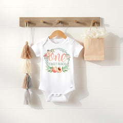Peach First Birthday.  Such a pretty first birthday bodysuit or t-shirt for your little one!  It features a delicate watercolor floral wreath with peach accents and the words "one sweet peach".  Since all of Bella Lexi™ designs are printed directly onto the garments of your choice, the designs won't peel, crack or fade!  This peach birthday design also makes a wonderful gift!  Your little peach will look adorable for her special day!